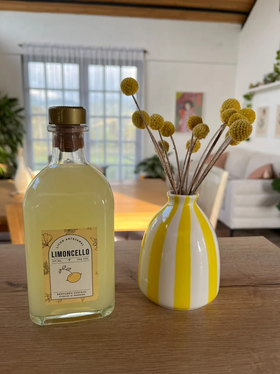 Botella de limoncello de la Destilería Cascajal sobre una mesa de madera, junto a un florero amarillo